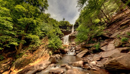 A scenic waterfall cascades down rocky cliffs, surrounded by lush green trees and a serene river below.