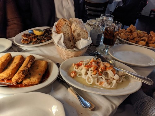 A table set with various dishes, including fried seafood, a seafood platter, bread, and drinks.