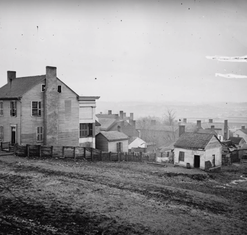 Black and white photo of a hillside with old houses and a dirt path, capturing a rural landscape.