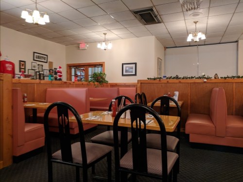 A cozy diner interior with pink booths, black chairs, and warm lighting, featuring tables set for dining.