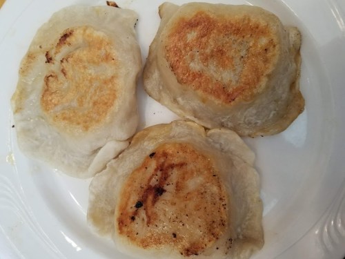 Three golden-brown pan-fried dumplings on a white plate, showcasing a crispy exterior.