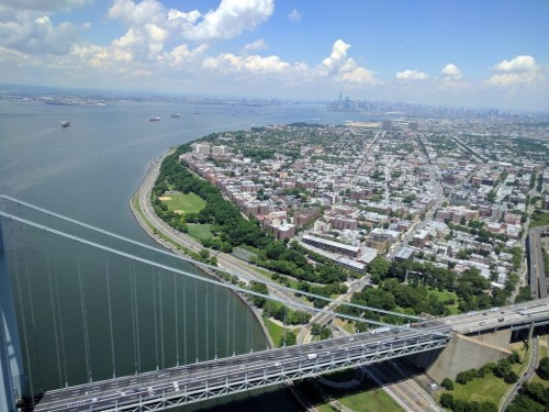 Aerial view of a river, cityscape, and green parks with a bridge crossing over the water on a sunny day.