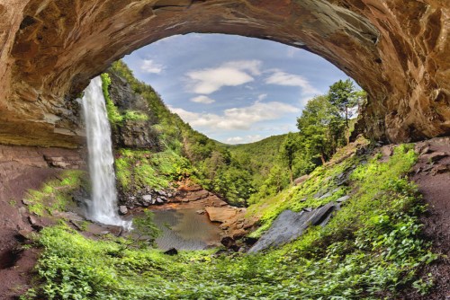 A panoramic view of a waterfall cascading into a lush green valley, framed by a rocky overhang.