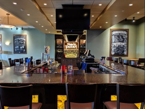 Interior of a Movie Tavern featuring a bar with stools, a large screen, and chalkboard menus on the walls.