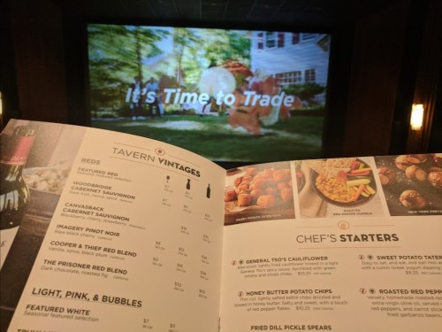 A menu open to the starters section, with a movie screen in the background displaying "It's Time to Trade."