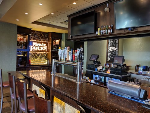 A bar area in a Movie Tavern, featuring a dark countertop, beer taps, and screens, with a cozy atmosphere.