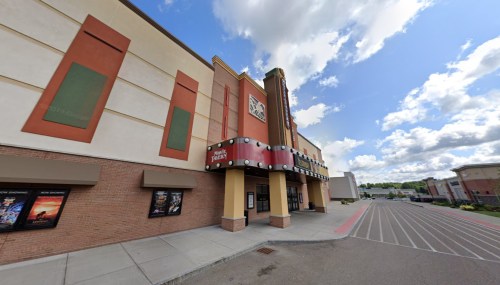Exterior view of a movie theater with colorful signage and a cloudy sky in the background.