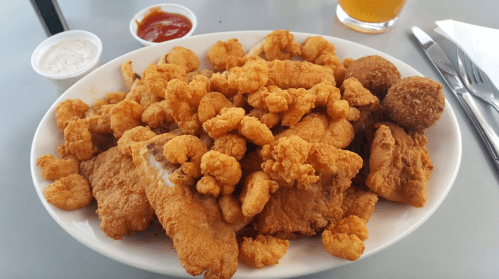 A large platter of fried seafood, including shrimp and fish, served with dipping sauces on the side.
