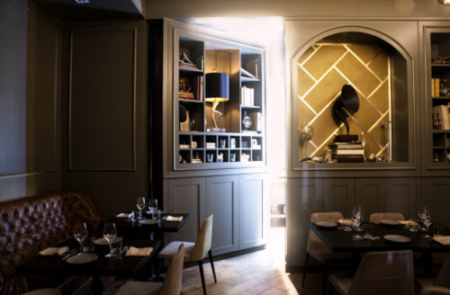 A dimly lit restaurant interior featuring elegant decor, wooden shelves, and tables set for dining.