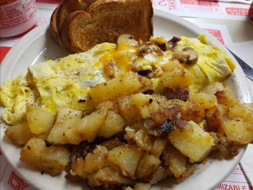 A plate of fluffy omelette with mushrooms, crispy hash browns, and two slices of toasted bread.