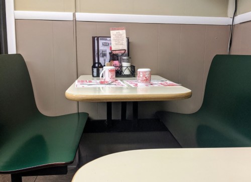 A small diner table with green chairs, menus, and condiments in a cozy, empty corner booth.