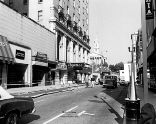 Black and white photo of a city street featuring the Hermitage theater and vintage cars parked along the road.