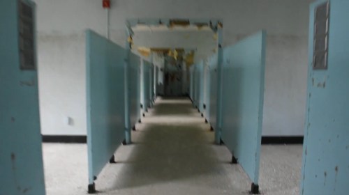 A long, empty corridor with blue partitions and peeling paint, creating an eerie, abandoned atmosphere.