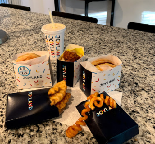 A variety of fast food items from Joyland, including sandwiches, chicken, curly fries, and a drink on a granite countertop.