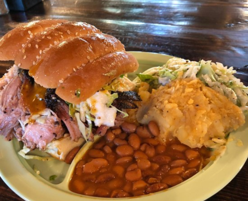 A pulled pork sandwich with coleslaw, served with mashed potatoes and baked beans on a plate.