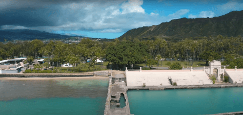 A scenic view of a coastal area with palm trees, a calm turquoise water body, and mountains in the background.