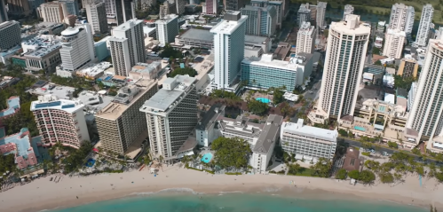 Aerial view of a coastal city with tall buildings and a sandy beach along the turquoise water.