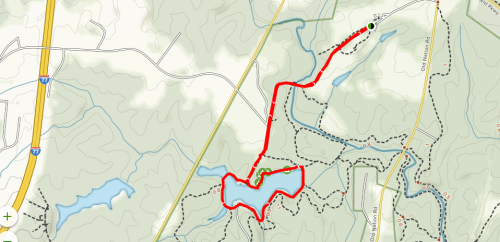 Map showing a winding red trail around a lake, with roads and paths marked in black and green.
