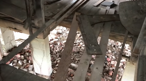 View of a dilapidated wooden floor with exposed beams and debris below, showcasing signs of decay and neglect.