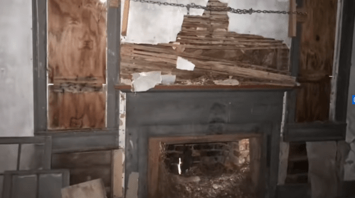An abandoned room with a broken fireplace, wooden boards, and peeling walls, creating a dilapidated atmosphere.
