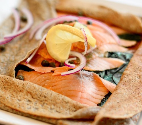 A savory galette filled with smoked salmon, capers, and red onion, garnished with lemon slices.
