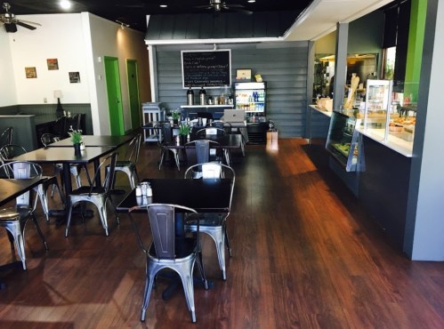 A cozy café interior with wooden floors, metal chairs, and a display counter in the background.