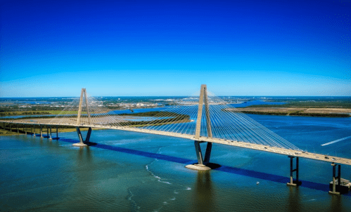 Aerial view of a modern suspension bridge spanning a blue river under a clear sky.