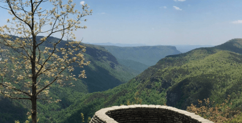 A scenic view of lush green mountains and valleys under a clear blue sky, with a stone overlook in the foreground.