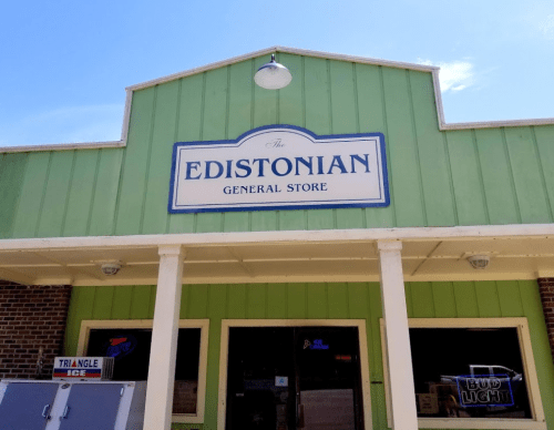 A green general store facade with a sign reading "The Edistonian General Store" and a clear blue sky above.