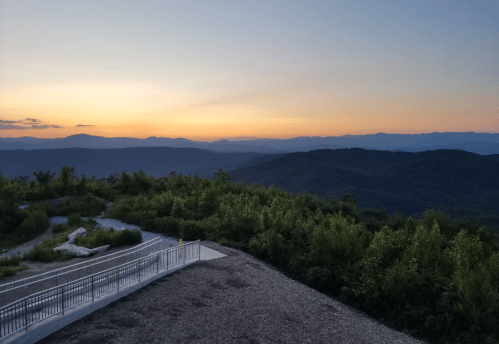 A scenic view of mountains at sunset, with a pathway and lush greenery in the foreground.