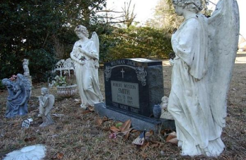 A gravestone surrounded by angel statues and decorative figures in a serene cemetery setting.
