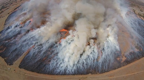 Aerial view of a large wildfire with thick smoke and flames engulfing the landscape.