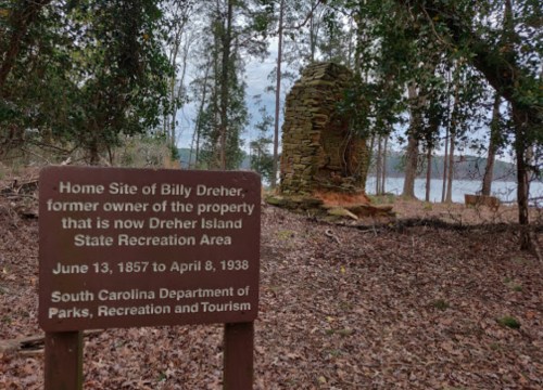 Sign marking the home site of Billy Dreher, with a stone structure and lake visible in the background.