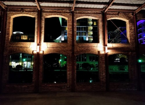 Nighttime view of brick arches with illuminated windows, showcasing a mix of urban architecture and greenery outside.