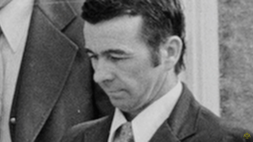 A black and white photo of a man in a suit, looking down with a serious expression.