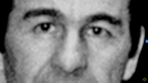 A blurred close-up of a man's face, focusing on his eyes and upper features.