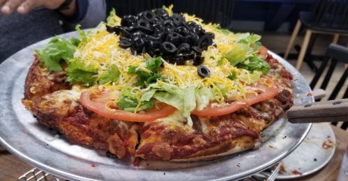 A colorful pizza topped with lettuce, tomatoes, cheese, and black olives on a metal serving tray.