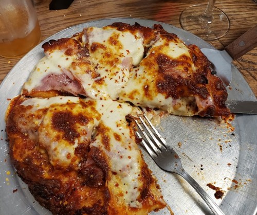 A close-up of a pizza with melted cheese, ham, and a crispy crust, partially sliced on a metal tray.