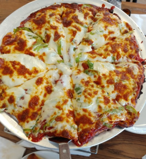A freshly baked pizza topped with melted cheese and green peppers, sliced into wedges on a silver serving tray.