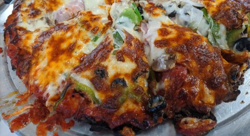 A close-up of a cheesy pizza topped with vegetables, meats, and a golden-brown crust, served on a metal tray.