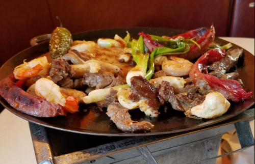 A sizzling platter of grilled meats and shrimp, garnished with green onions and peppers.