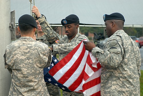 Soldiers in uniform carefully raise the American flag during a ceremony.