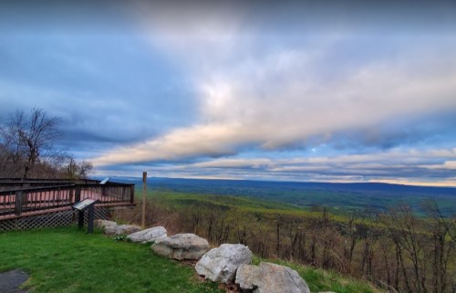 A scenic view from a lookout point, featuring rolling green hills under a cloudy sky.
