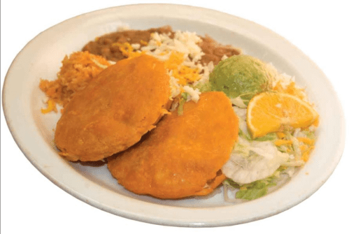A plate of two golden fried tacos, served with rice, beans, lettuce, guacamole, and a slice of orange.
