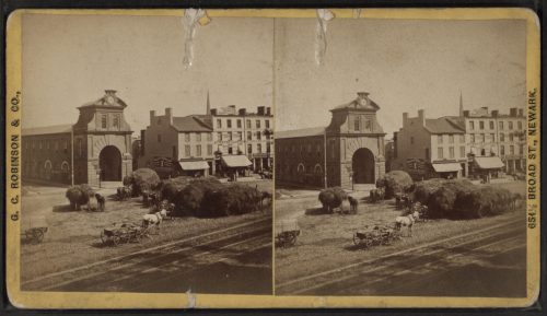 Historic photo of a street scene in Newark, featuring buildings, horse-drawn carriages, and a large archway.