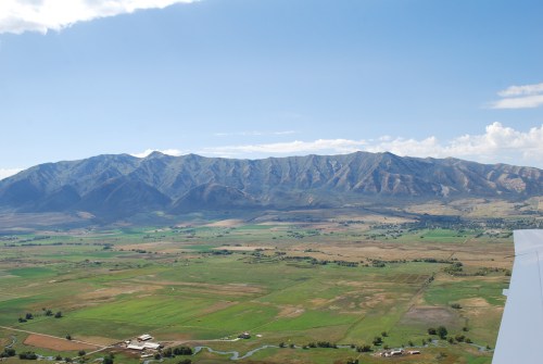 Aerial view of green fields and mountains under a clear blue sky, with a winding river in the foreground.