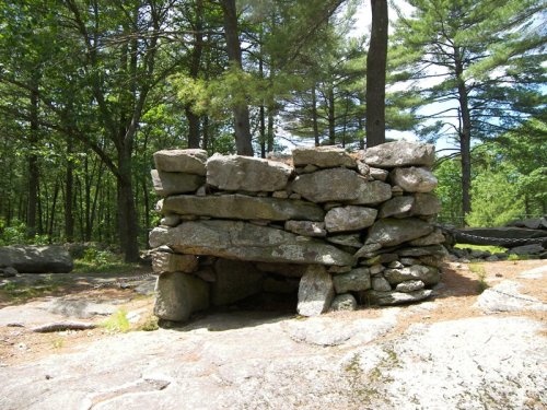 A stone structure made of large rocks, surrounded by trees in a wooded area.
