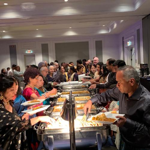 A diverse group of people serving themselves from a buffet at a festive event, with various dishes displayed.
