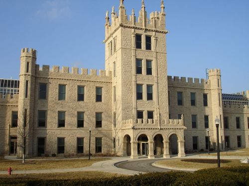 Historic stone building with castle-like architecture, featuring towers and arched entrances, set against a clear blue sky.