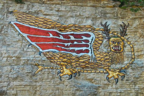 A colorful mural of a mythical creature with wings and claws painted on a rocky cliff face.